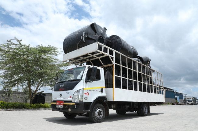 A lorry in the factory yard loaded with large black Jumbo cylindrical tanks, stacked above the cab behind a WIDE LOAD sign and ready to leave.